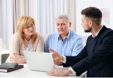 A senior man and a middle-aged woman discuss paperwork with a suited professional in an office.